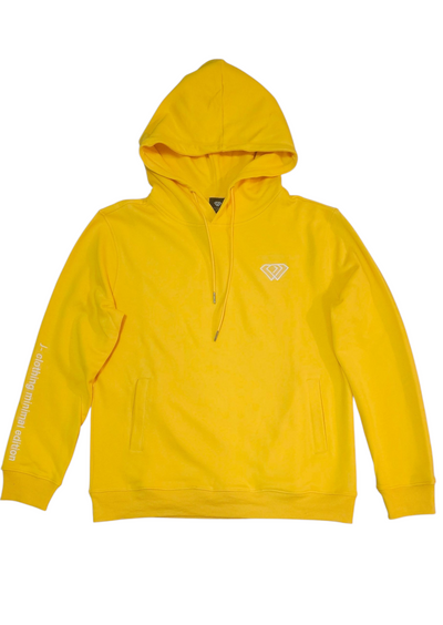 A woman with curly hair walks confidently down a tree-lined sidewalk on a sunny autumn day, wearing a J-clothing premium cotton yellow pullover hoodie and classic blue jeans that elevate her streetwear style.