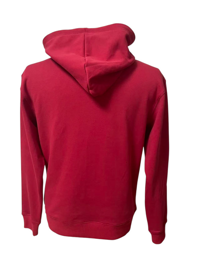 A man with short dark hair and a beard walks on a city street wearing a red J-clothing premium cotton hoodie, blue jeans, and white sneakers. The background is slightly blurred, showing buildings and outdoor seating.