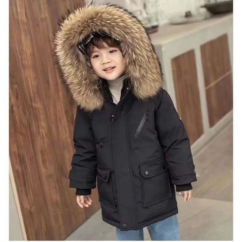 A young child sporting a Jstoremart red coat with a fur-lined hood and black beanie stands indoors. This stylish boys' winter jacket by Jstoremart features multiple pockets and black accents. The child looks sideways, framed by wooden panels and some equipment in the background.